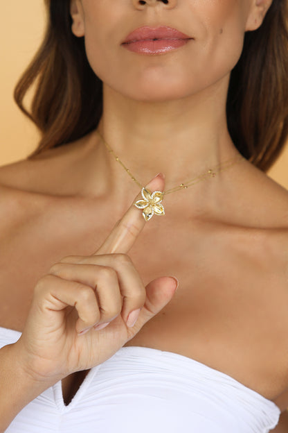 Woman wearing Frangipani gold necklace  designed by Renée Chamoun against a beige background