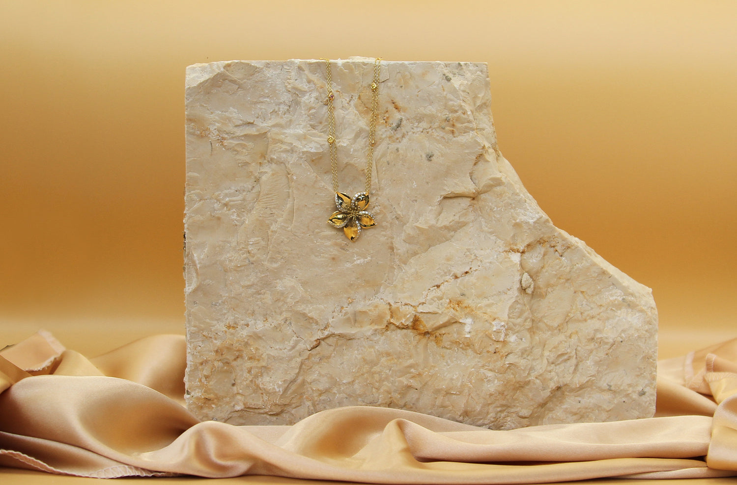 Frangipani gold necklace designed by Renée Chamoun against a marble stone