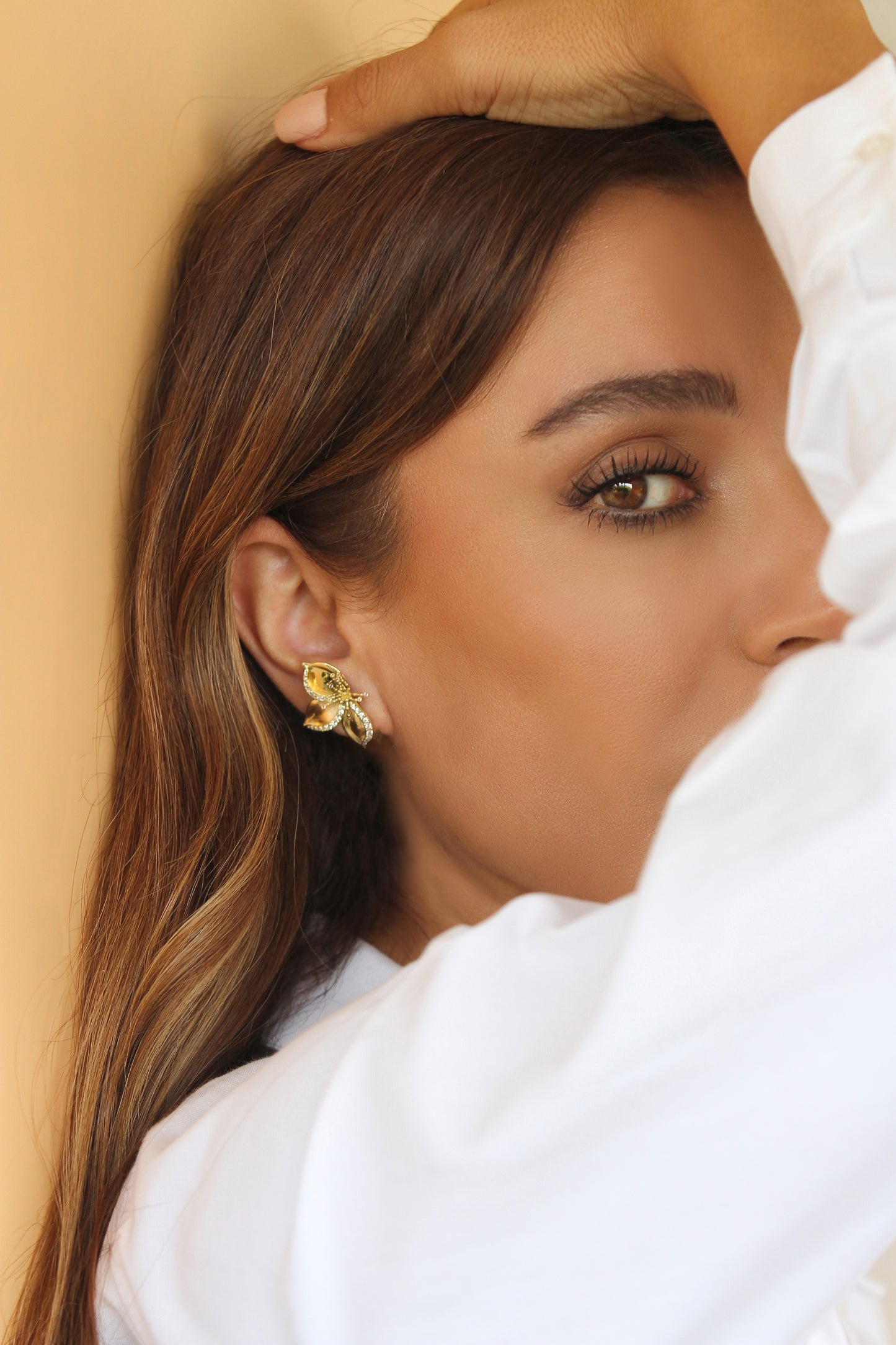 Close-up of a woman wearing gold Frangipani earrings designed by Renée Chamoun against a beige background