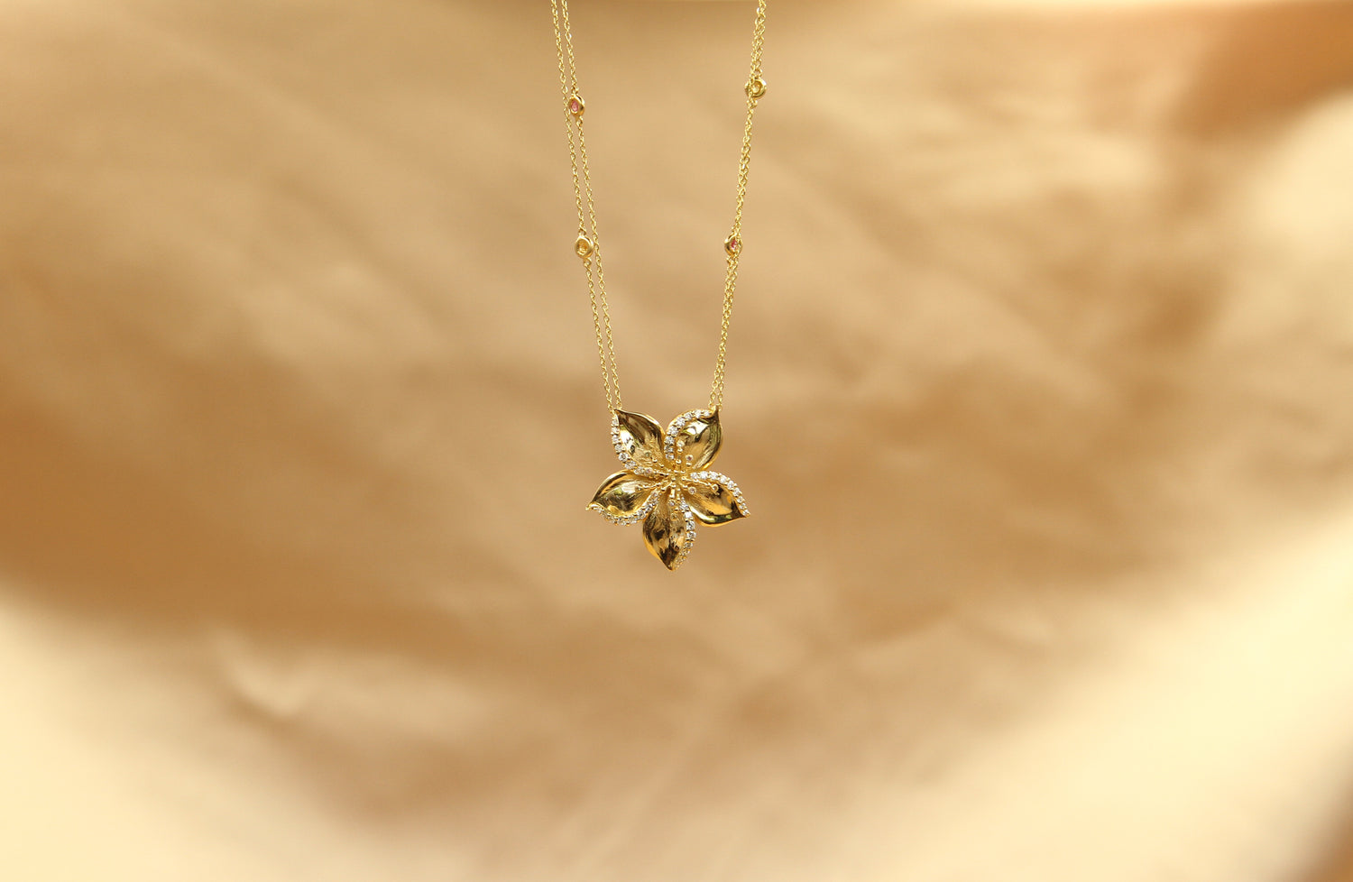 Frangipani gold necklace designed by Renée Chamoun against a soft beige background