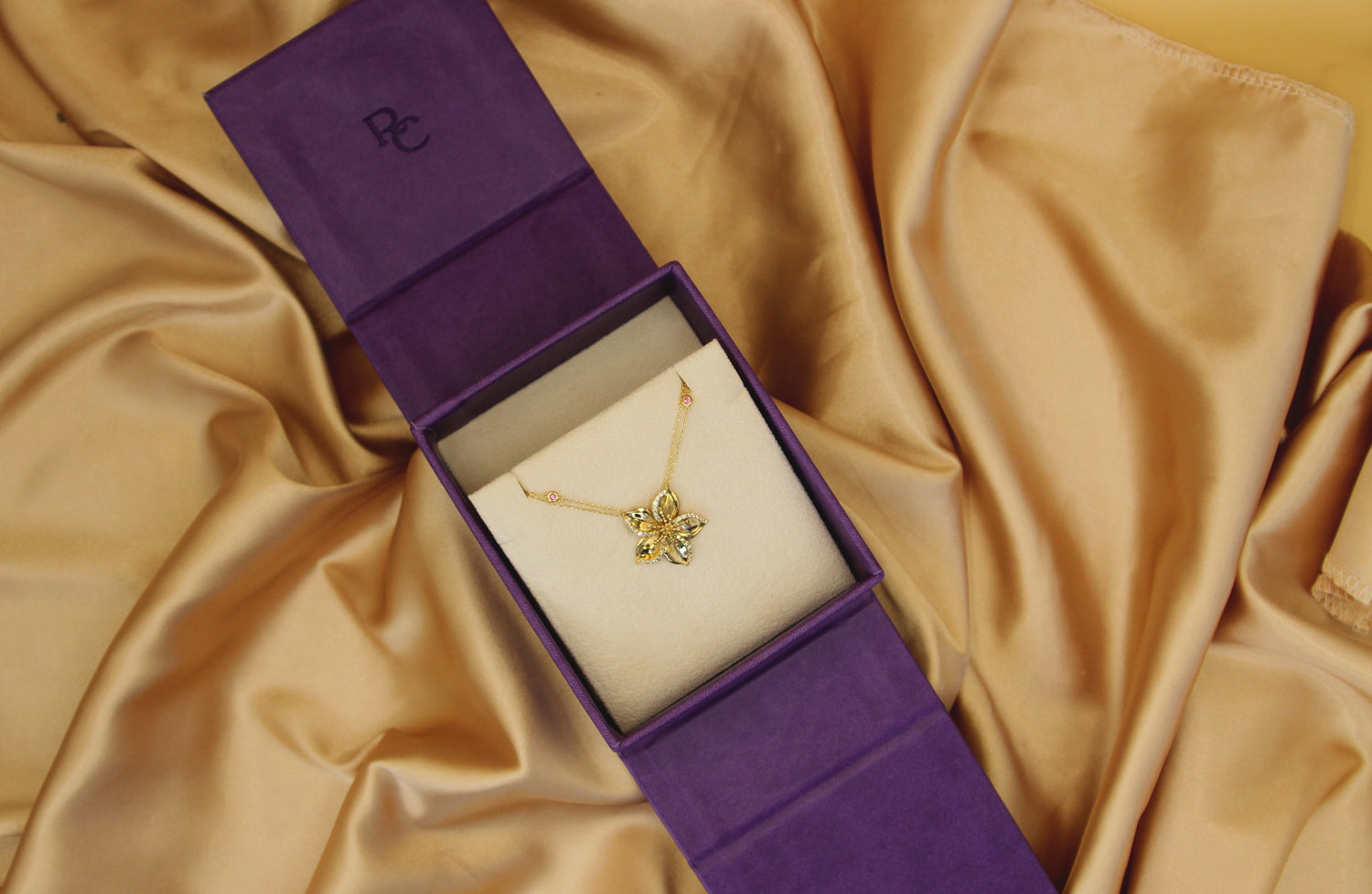Frangipani gold necklace designed by Renée Chamoun placed in a purple jewelry box against fabric background