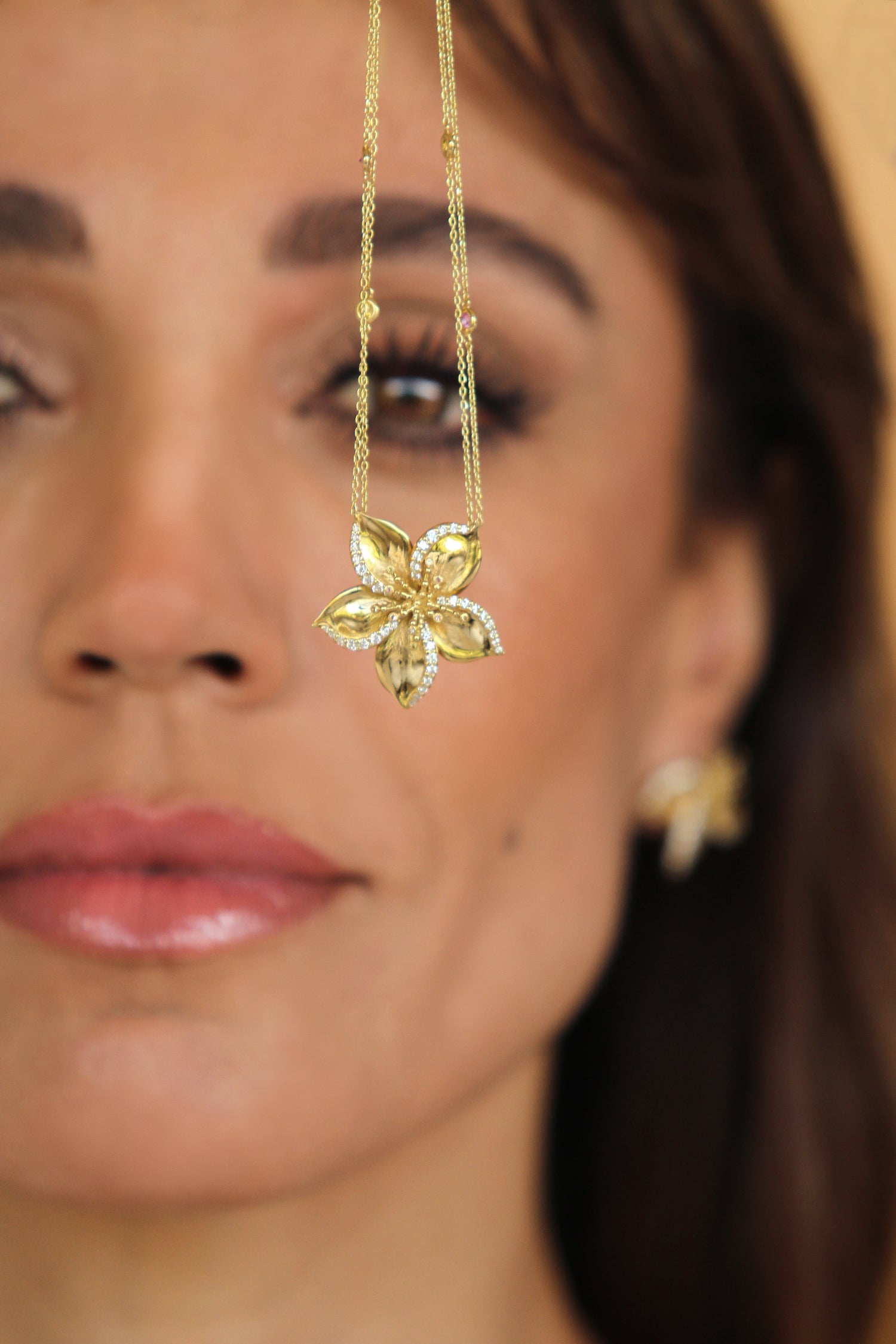 Close-up of a woman holding a gold Frangipani necklace designed by Renée Chamoun